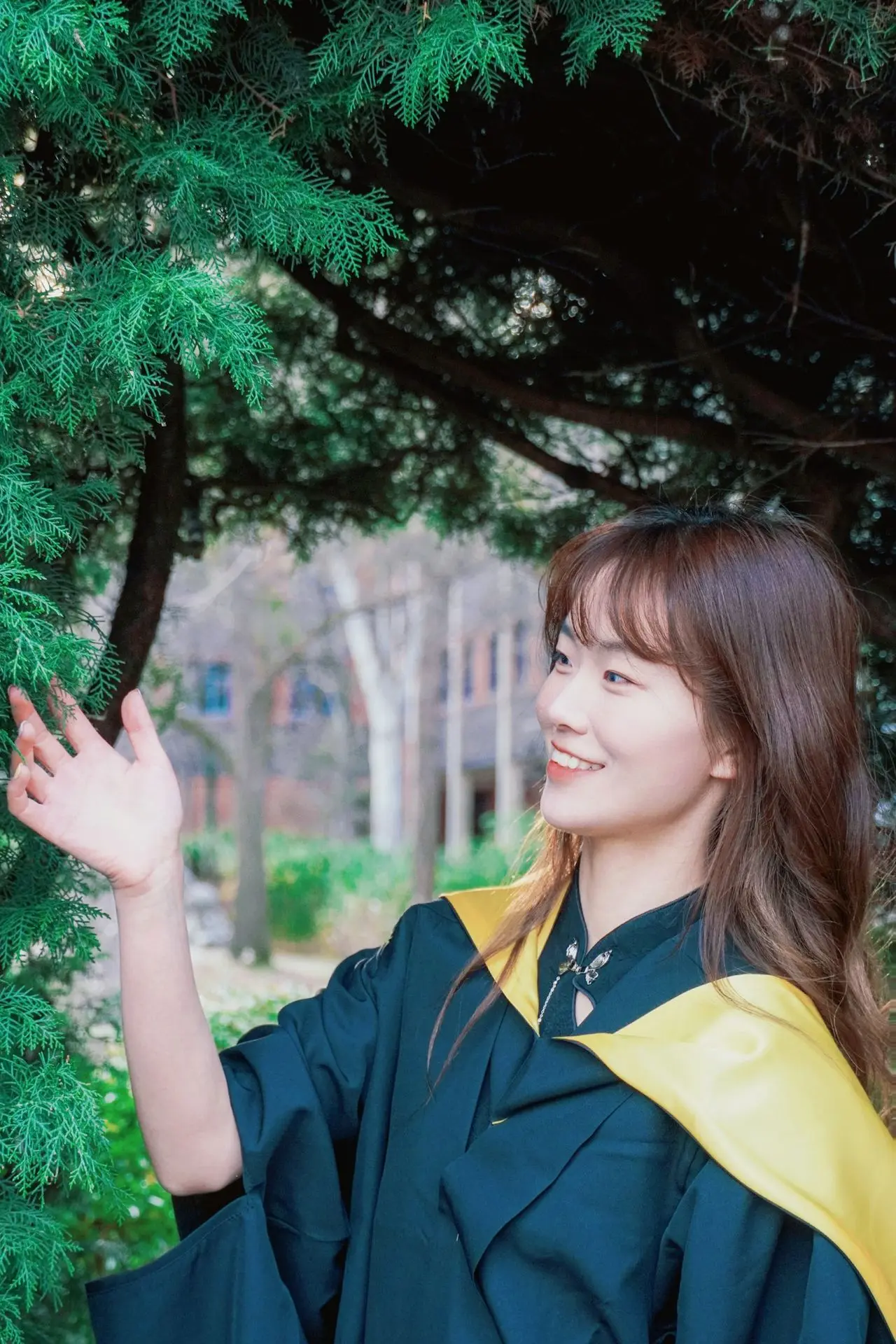 A woman in a graduation gown is standing in front of a tree